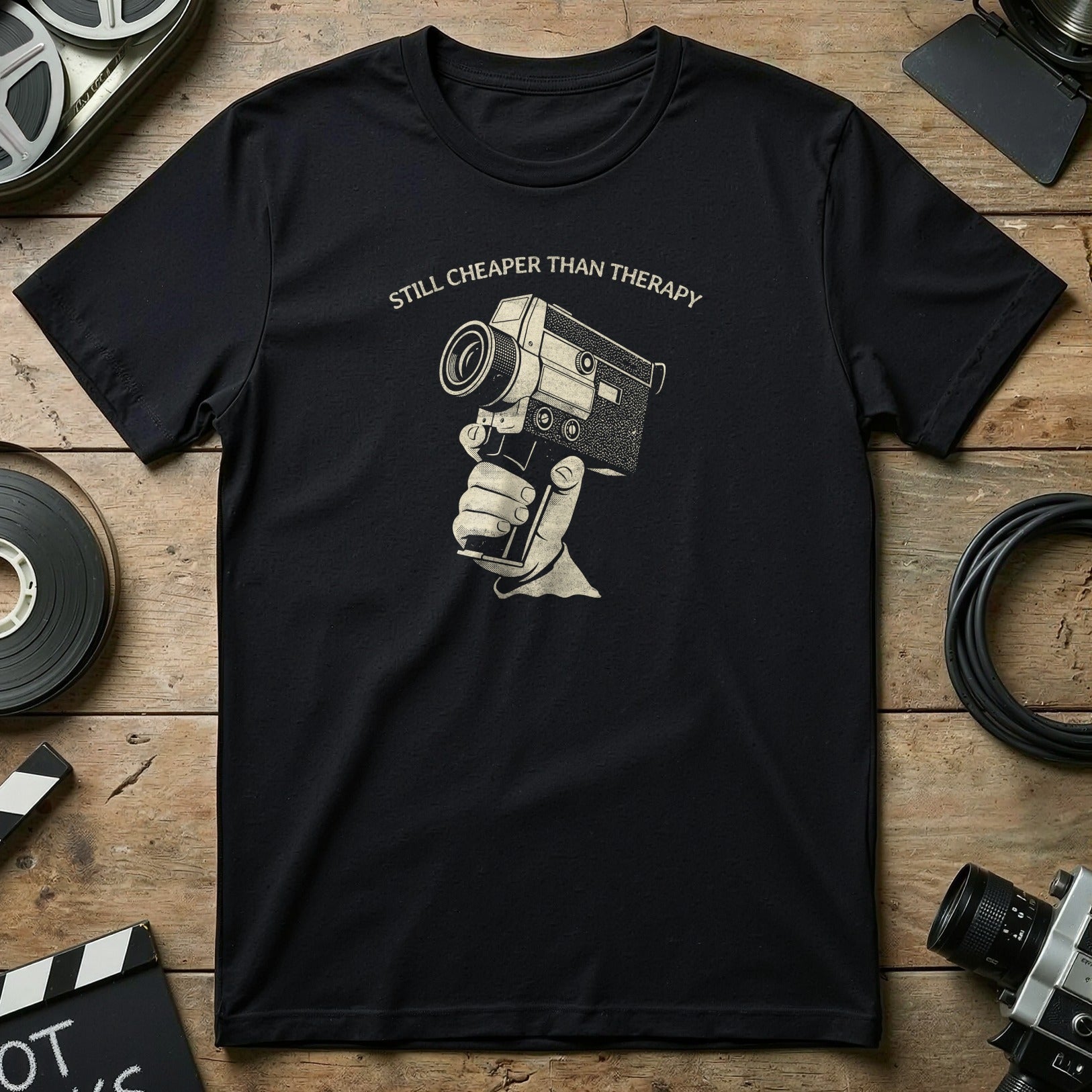 Black t-shirt with "Still Cheaper Than Therapy" text and vintage camera graphic.