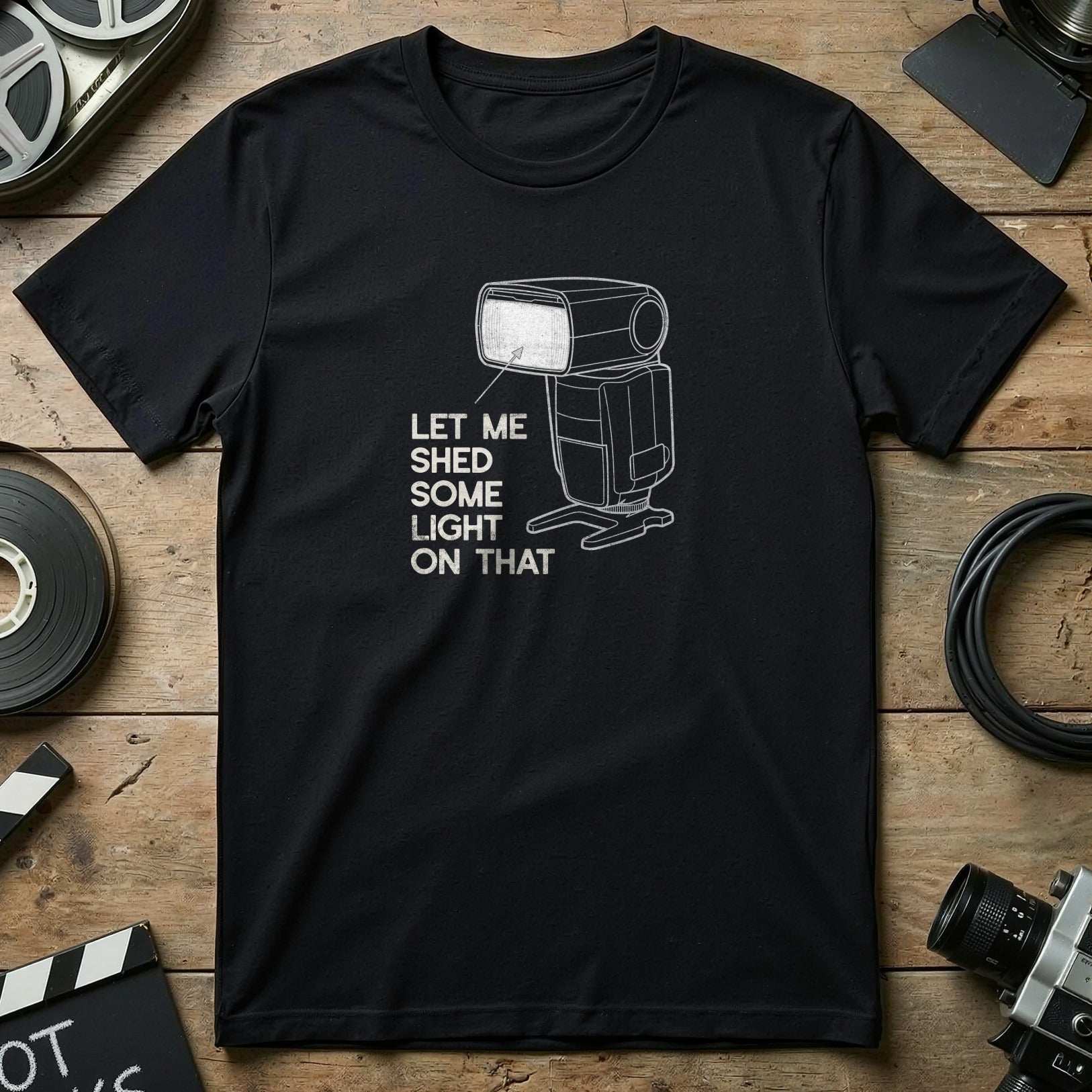 Black t-shirt with a white outline of a camera flash and text "Let Me Shed Some Light On That".